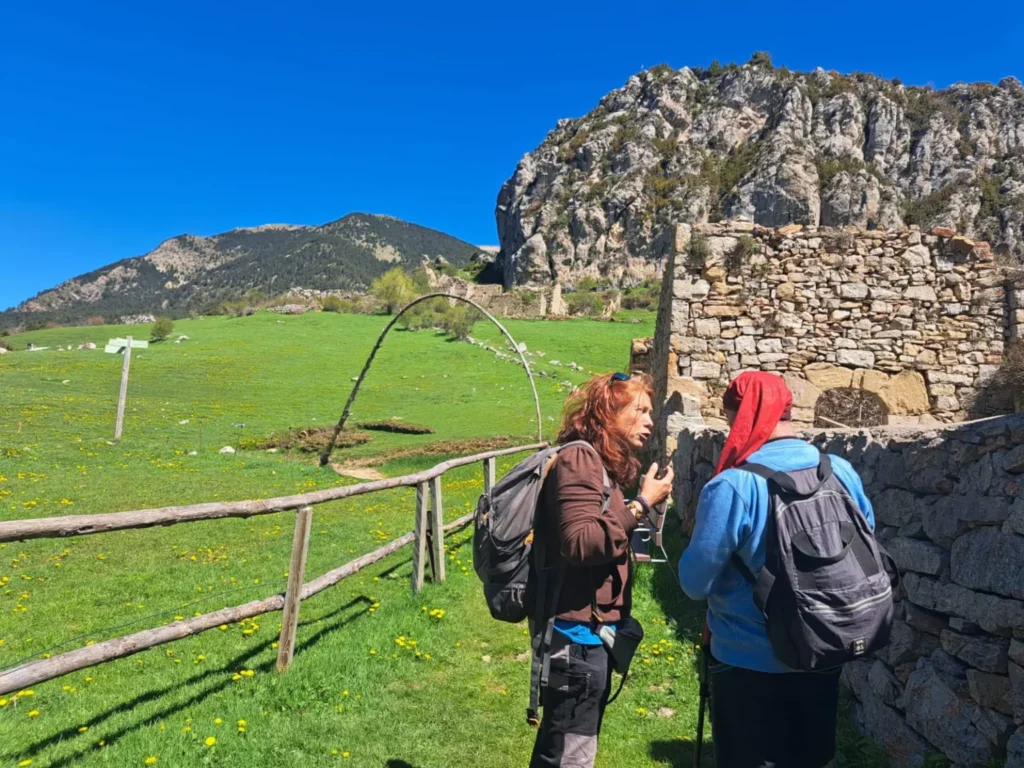Gemma Roselló, guiando a un persona por la montaña a través de un pasto verde y un bonito paisaje soleado